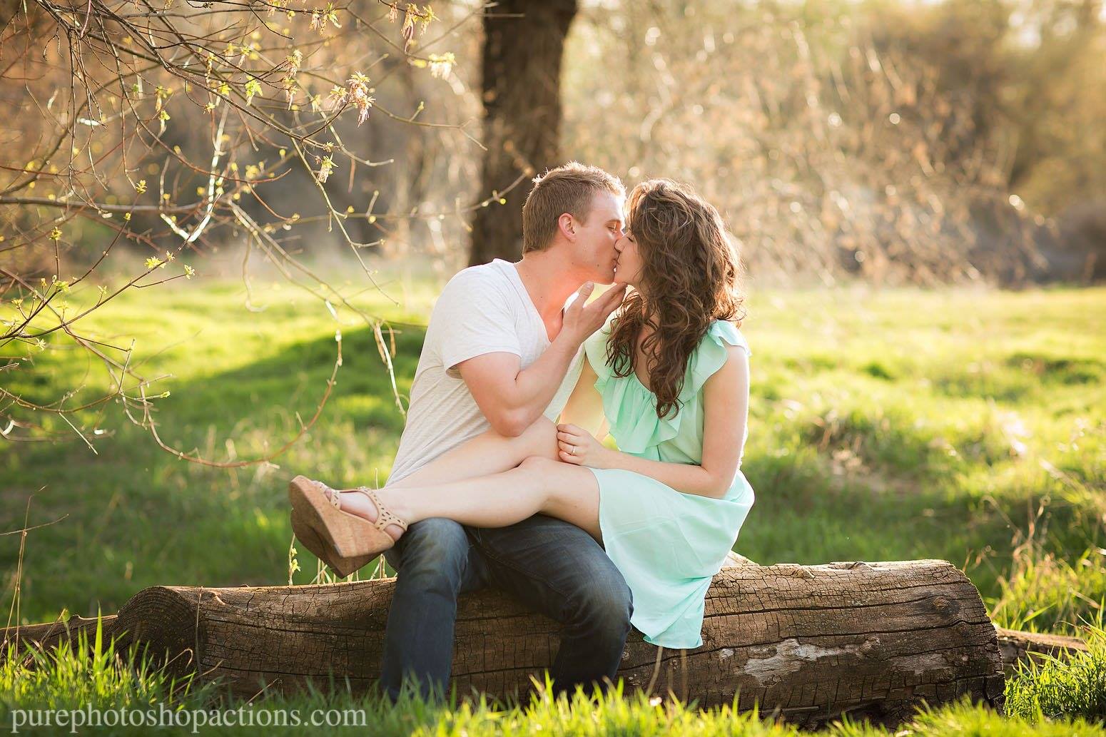 An image of a couple cuddling and kissing on a log in tall grass edited using Pure Essential Edit Photoshop Actions and Lightroom Presets.