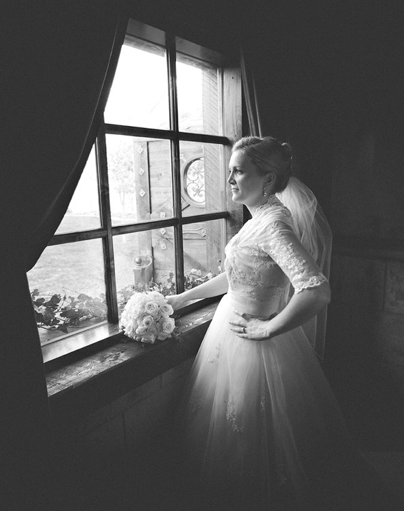 An image of a bride standing at an old fashioned window with her bouquet. Edited using Pure Lightroom Presets Volume 1.