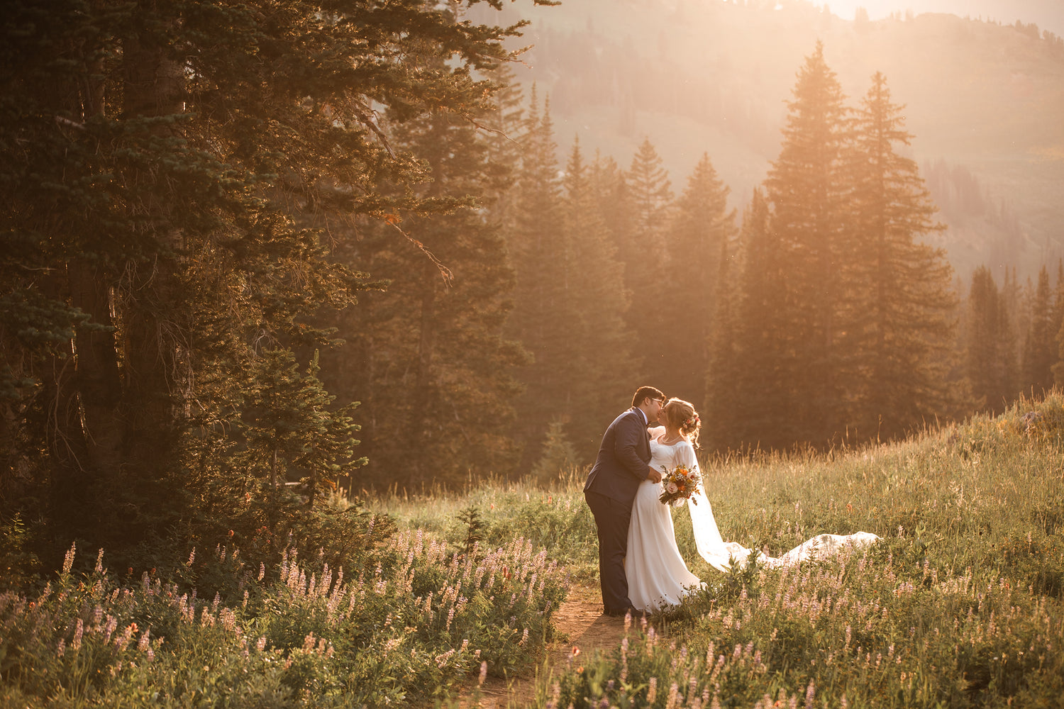 Couple embracing in a field with mountains and trees in the background