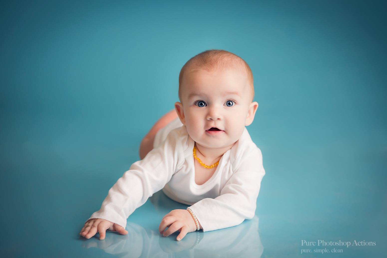 A photo of a baby on a seamless blue background demonstrating the Pure Retouch Photoshop technique using Photoshop Actions and Instructional videos.  The skin is very smooth and the tone is even and the blue background has no wrinkles or seams.