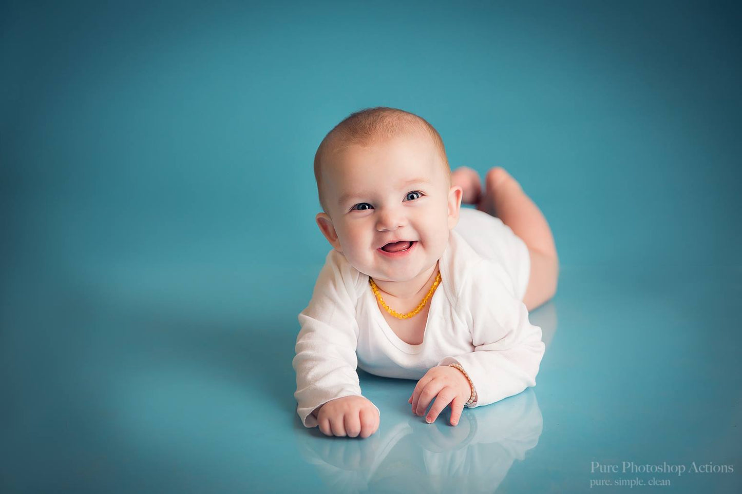 A photo of a baby on a seamless blue background demonstrating the Pure Retouch Photoshop technique using Photoshop Actions and Instructional videos.  The skin is very smooth and the tone is even and the blue background has no wrinkles or seams.