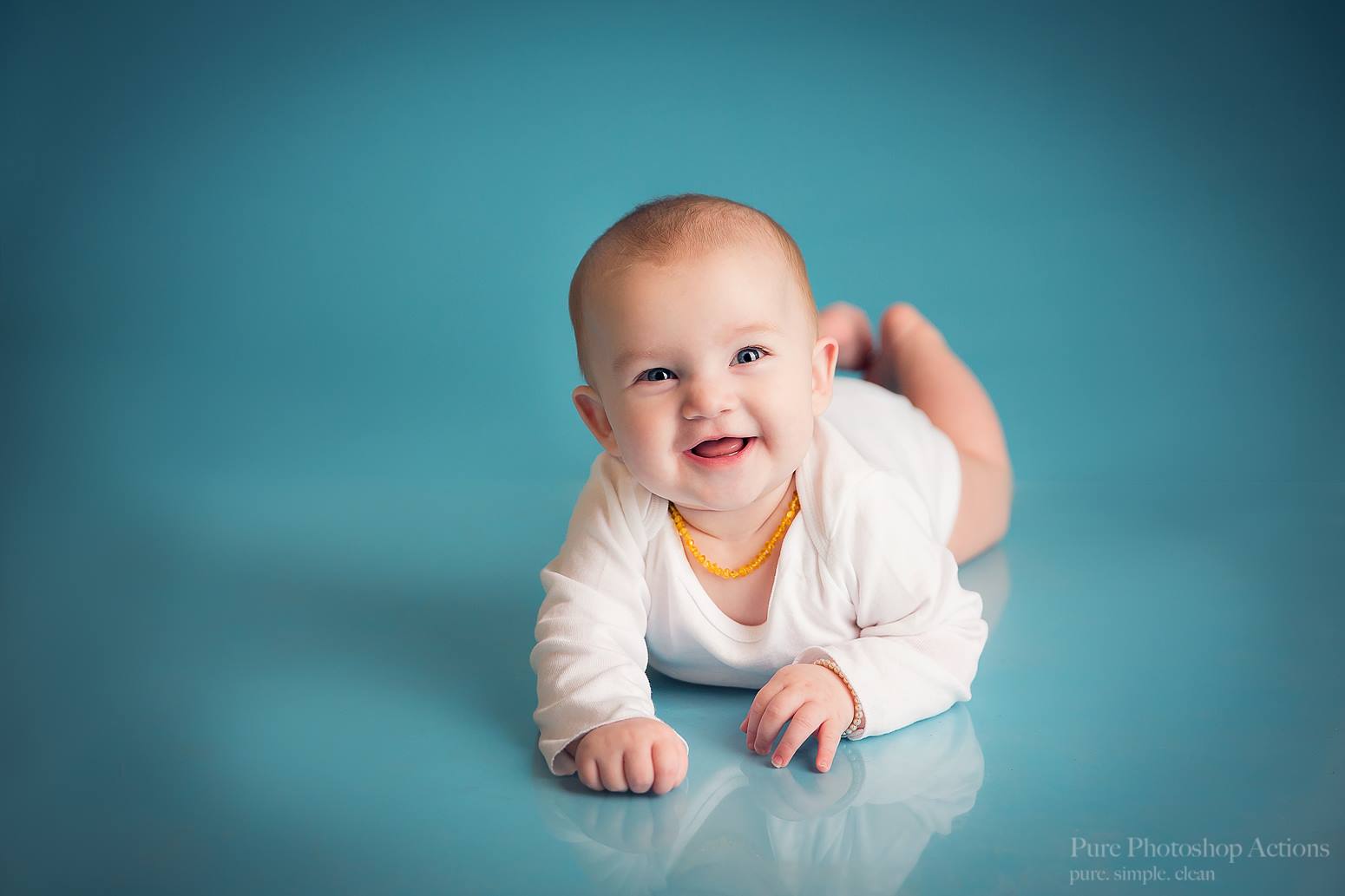 A photo of a baby on a seamless blue background demonstrating the Pure Retouch Photoshop technique using Photoshop Actions and Instructional videos.  The skin is very smooth and the tone is even and the blue background has no wrinkles or seams.