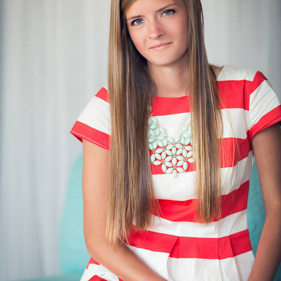 A young woman in a striped dress sitting in a blue chair against a white curtain demonstrating the Pure Retouch technique with creamy, flawless skin.