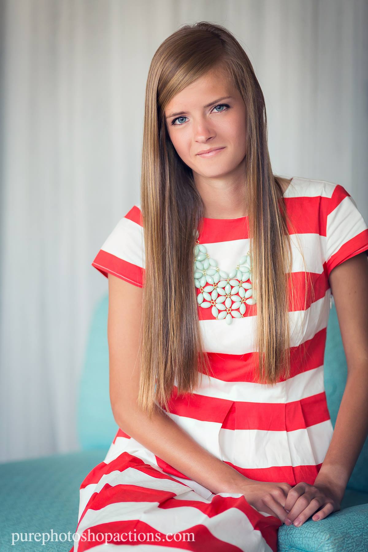 A young woman in a striped dress sitting in a blue chair against a white curtain demonstrating the Pure Retouch technique with creamy, flawless skin.