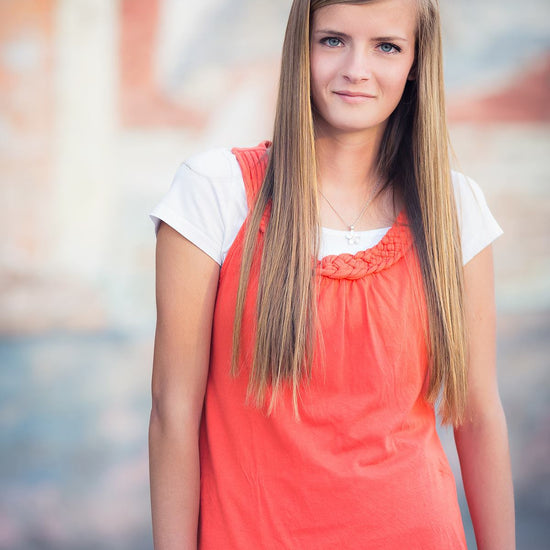A young woman in a coral top outside demonstrates the Pure Retouch skin retouching technique for Photoshop with creamy, flawless skin.