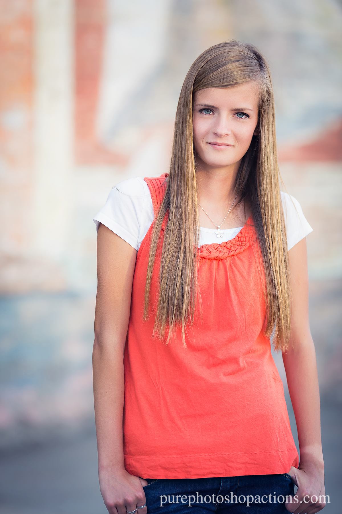 A young woman in a coral top outside demonstrates the Pure Retouch skin retouching technique for Photoshop with creamy, flawless skin.