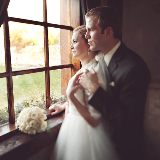 An image of a couple standing before an old fashioned window holding a bouquet with a dreamy soft edit.