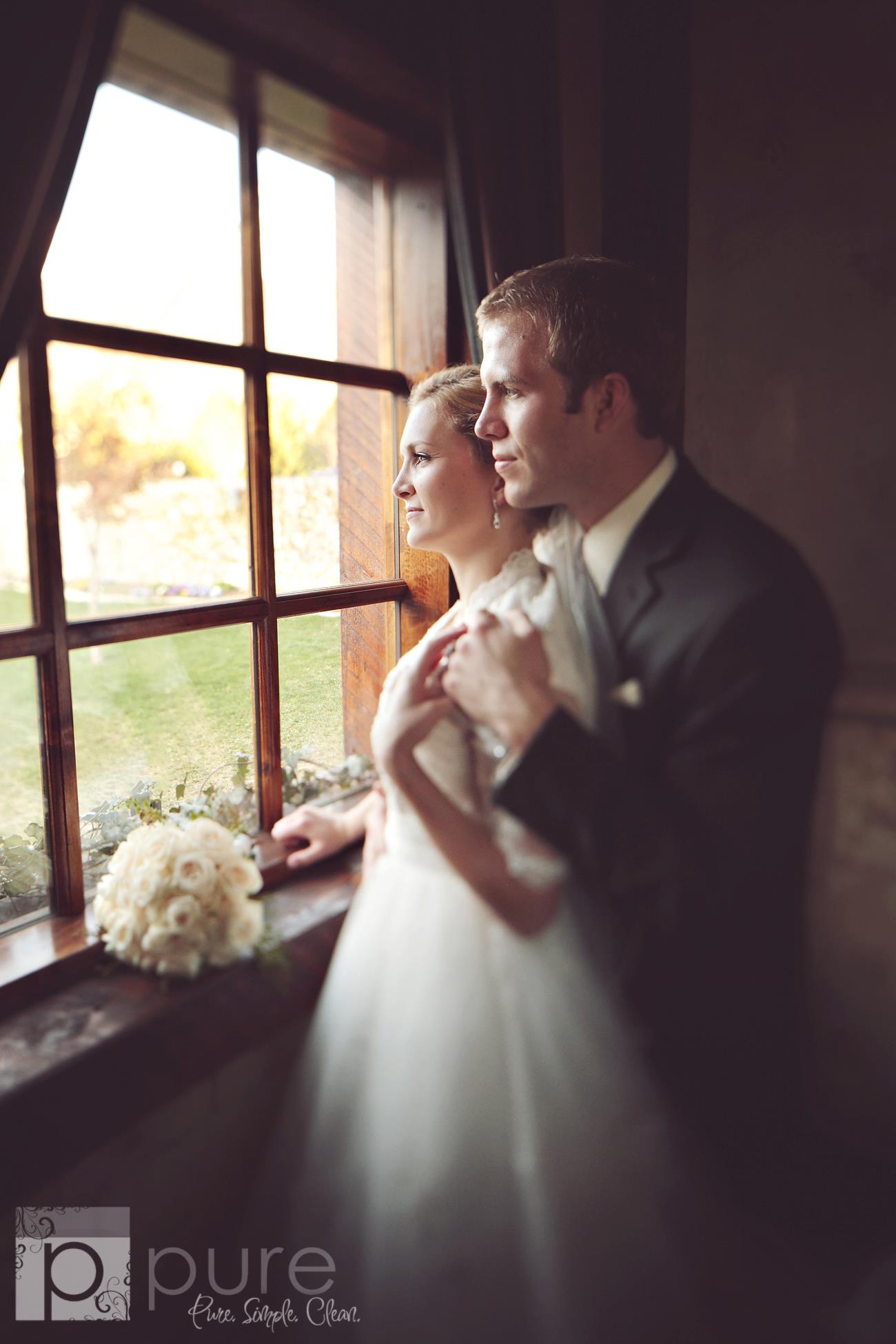 An image of a couple standing before an old fashioned window holding a bouquet with a dreamy soft edit.
