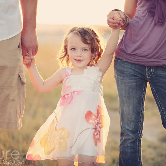 A Vintage toned image of a couple holding a little girl's hands in a dreamy field location edited using Purely Vintage Photoshop Actions.