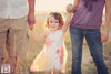 A Vintage toned image of a couple holding a little girl's hands in a dreamy field location edited using Purely Vintage Photoshop Actions.